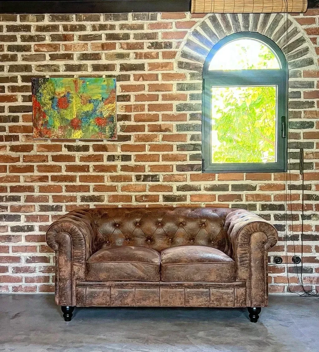 Sofá Chesterfield de cuero con pared de ladrillo y ventana de arco